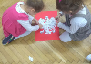 2 dziewczynki ozdabiają godło Polski białymi skrawkami papieru.